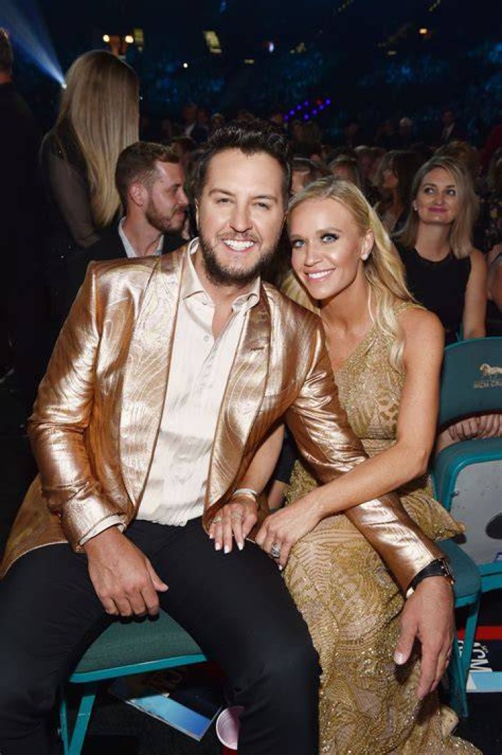 Caroline Boyer in a white jumpsuit in the red carpet with suit-clad Luke Bryan