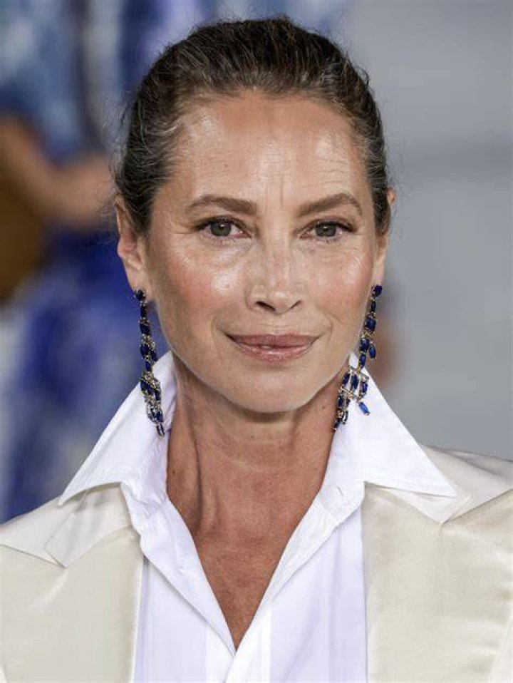 Christy Turlington walking in a gold one-shoulder dress 