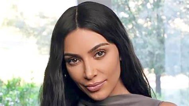 Kim Kardashian poses near some of her shapewear, she is wearing sunglasses and is dressed in bright pink