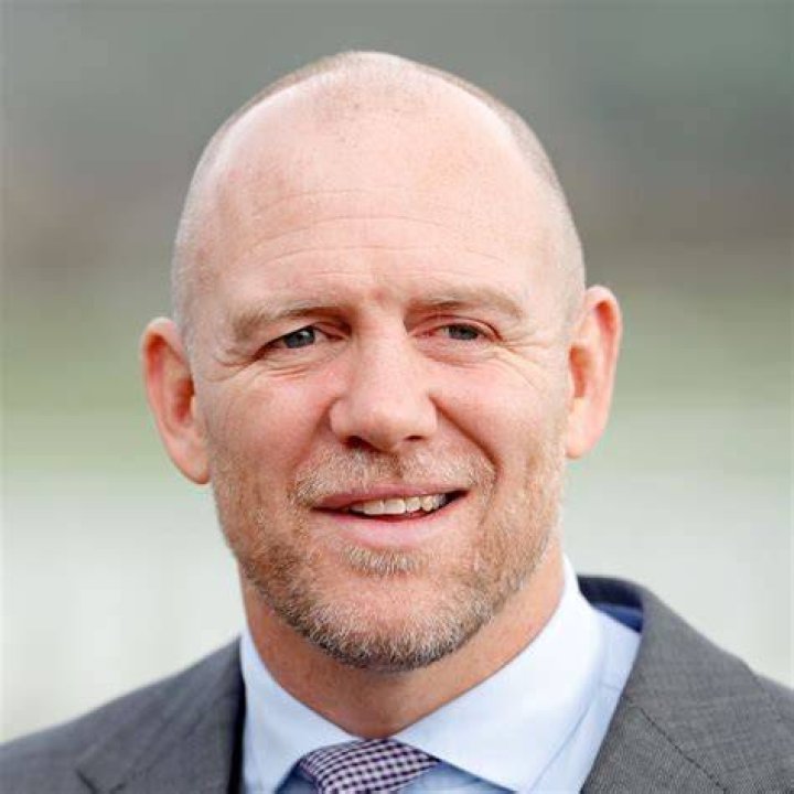 Mike Tindall in a suit and Zara Tindall in a purple dress. The pair are stood on a rugby pitch