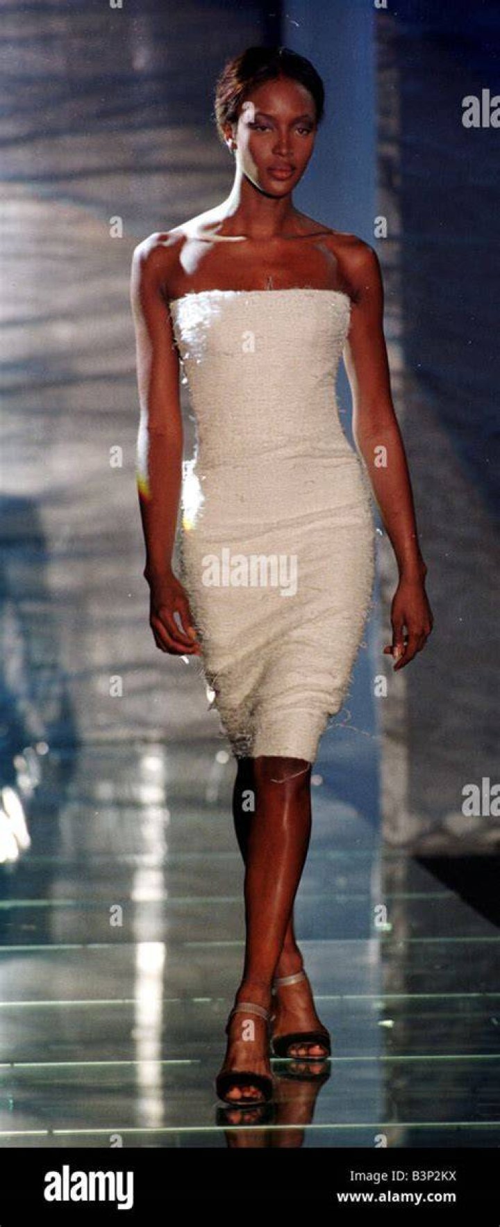 Naomi Campbell wearing a white babydoll mini dress, a fluffy pink bolero and a feather headpiece 